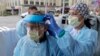 Tilliesa Banks, right, an emergency services nurse at Harborview Medical Center in Seattle, helps a colleague put on a medical face shield prior to their shift in a triage tent outside the Harborview emergency department.