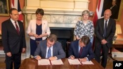Britain's Prime Minister Theresa May, second right, stands with First Secretary of State Damian Green, right, Democratic Unionist Party leader Arlene Foster, second left, and DUP Deputy Leader Nigel Dodds as DUP MP Jeffrey Donaldson, sitting left, and Government Chief Whip Gavin Williamson sign documents inside 10 Downing Street in London, June 26, 2017. 