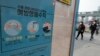 Para pejalan kaki mengenakan masker mendekati halte bus yang ditempeli poster peringatan bahaya pandemi corona di Seoul, Korea Selatan, 25 Mei 2020.