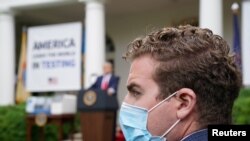 Seorang anggota staf Presiden Donald Trump mengenakan masker wajah di Rose Garden saat Trump memberikan keterangan pers tentang Covid-19 di Gedung Putih, Wasington, 11 Mei 2020.