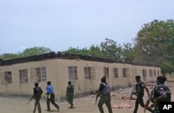 FILE - Security personnel walk past a burnt-out government secondary school in Chibok, where gunmen abducted more than 200 students, Chibok, Nigeria, April, 21, 2014.