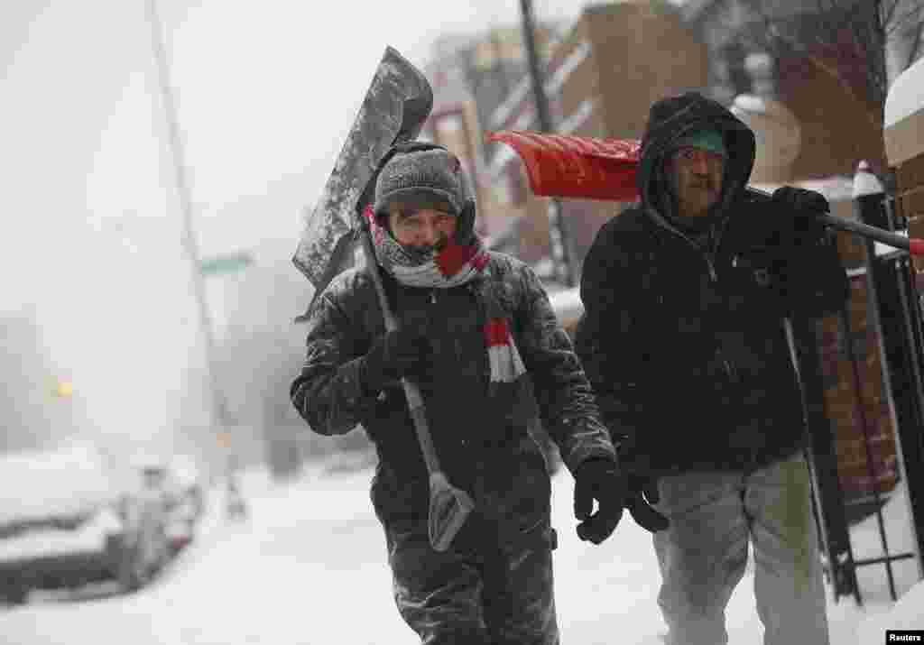 Two men carry shovels as they walk along through several inches of snow in Detroit, Michigan, Jan. 2, 2014. 