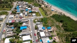 FILE - An aerial photo of the Viequez neighborhood, east of San Juan, Puerto Rico, where people were still living in damaged homes, protected by blue plastic tarps, months since Hurricane Maria devastated the island, June 18, 2018.