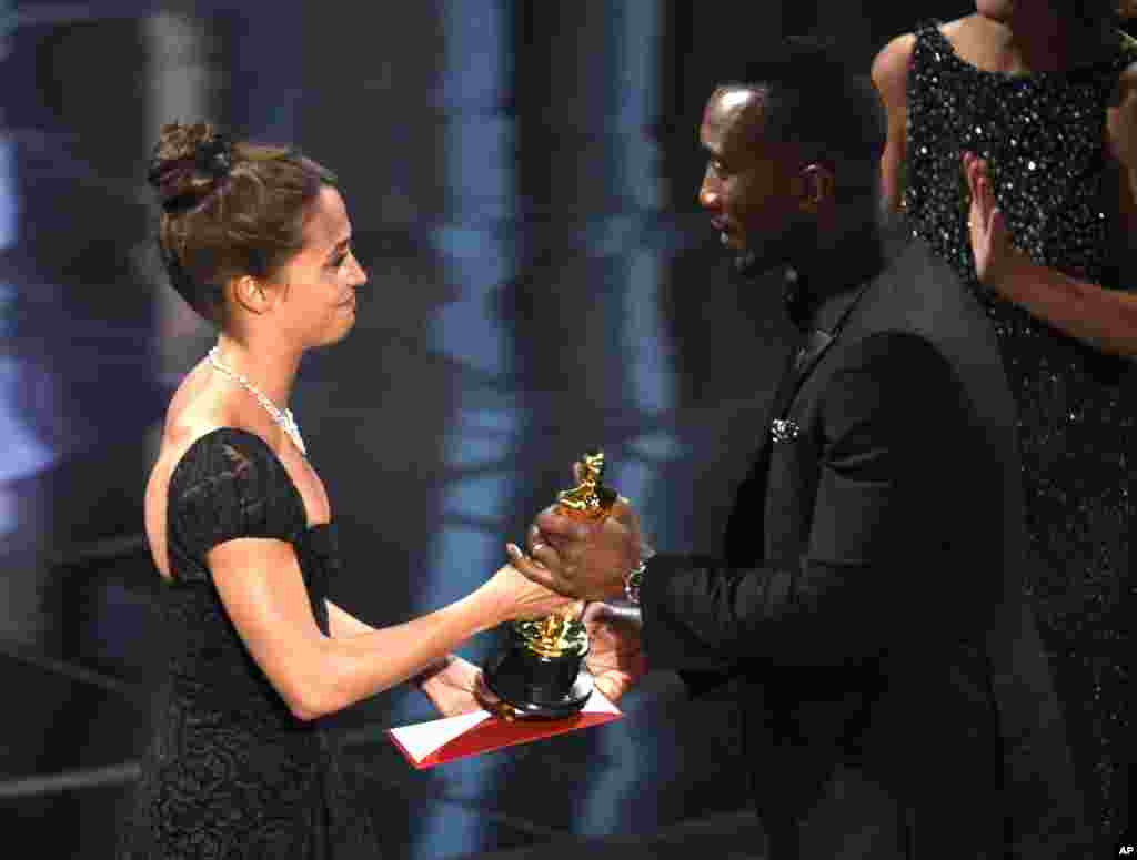 Mahershala Ali (kanan) dari film "Moonlight" menerima piala aktor pendukung terbaik Oscar 2017 dari aktris Alicia Vikander, dalam cara di Dolby Theatre (26/2) di Los Angeles. 
