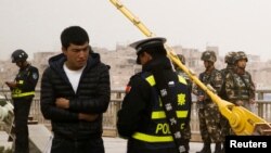Seorang polisi memeriksa kartu identitas seorang pria sementara pasukan keamanan berjaga di sebuah jalan di Kashgar, Wilayah Otonomi Xinjiang Uighur, China, 24 Maret 2017. 