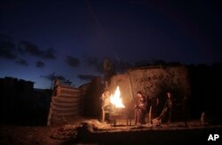 A Palestinian family warm themselves up with a fire outside their makeshift house during a power cut in a poor neighborhood in town of Khan Younis in the southern Gaza Strip, Jan. 15, 2017.
