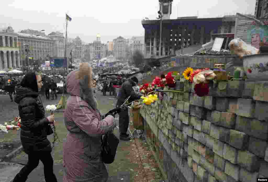 Dua perempuan bersiap meletakkan bunga di dinding Alun-alun Kemerdekaan di Kyiv (22/2).