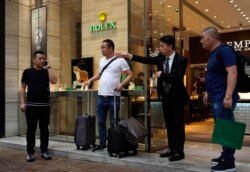 FILE - A salesman of a watch shop directs the way to find a taxi for a group of mainland tourists in a shopping district in Hong Kong, Oct. 30, 2019.