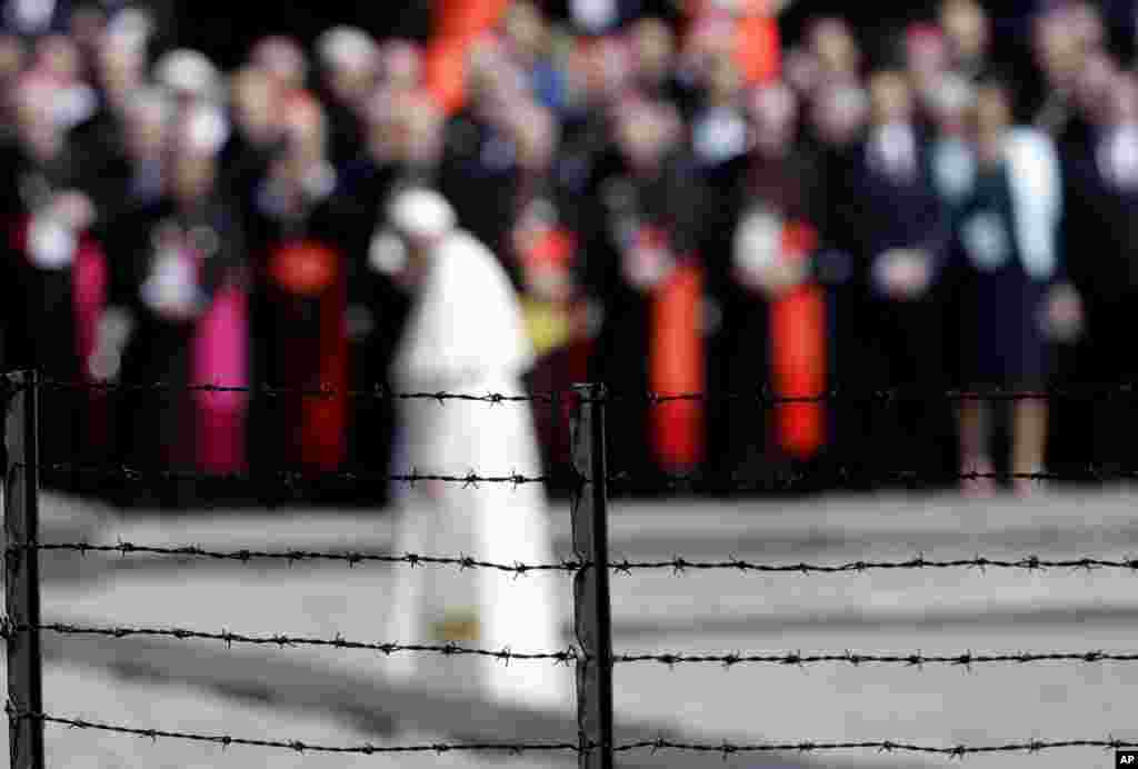 Pope Francis, background, is framed by a barbed wire as he prays in front of the memorial at the former Nazi death camp Auschwitz-Birkenau, in Oswiecim, Poland. Francis paid a somber visit to the camp Friday, becoming the third consecutive pontiff to make the pilgrimage to the place where Adolf Hitler's forces killed more than 1 million people, most of them Jews.