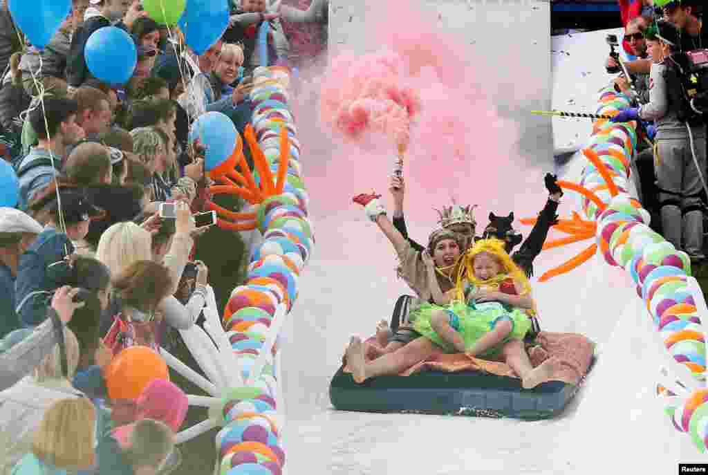 Participants hold smoke flares as they slide down along a chute to cross a pool of water and foam during the "Letniy Gornoluzhnik" (Summer mountain puddle rider) festival at the Bobroviy Log Fun Park near the Siberian city of Krasnoyarsk, Russia.