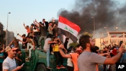 Anti-government protesters take over an armored vehicle before they burn it during a demonstration in Baghdad, Oct. 3, 2019. 