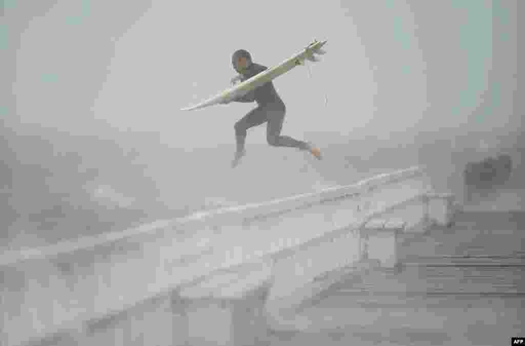 A surfer jumps off the pier into Port Phillip Bay to take advantage of the waves as a storm lashes the Melbourne area, Australia.