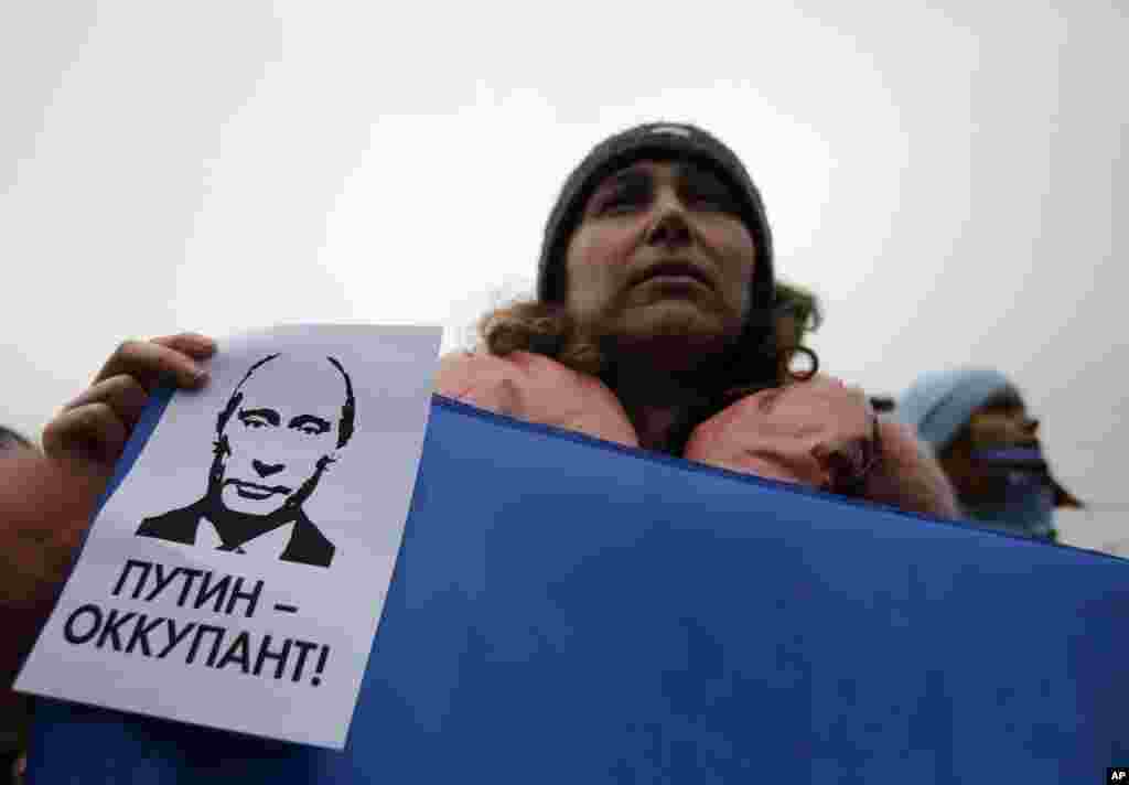 Seorang perempuan memegang poster bertuliskan "Putin adalah Penjajah" dalam kampanye anti-pemecahan Ukraina di Simferopol, Krimea, Ukraina (11/3). (AP/Darko Vojinovic)