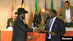 South Sudan's President Salva Kiir (front L) and South Sudan's rebel commander Riek Machar exchange documents after signing a cease-fire agreement during the Inter Governmental Authority on Development (IGAD) Summit on the case of South Sudan in Ethiopia'