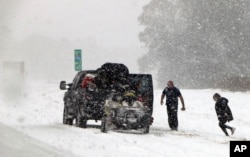 People attend to their vehicle on Interstate 26, near Savannah, Ga., Jan. 3, 2018. A brutal winter storm dumped snow in Tallahassee, Fla., Wednesday for the first time in nearly three decades before slogging up the Atlantic coast.