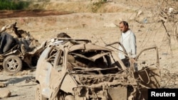 FILE - An Afghan man inspects the wreckage of a car at the site of a truck bomb blast in Ghani Khel district of Nangarhar province, Afghanistan, Oct. 3, 2020.