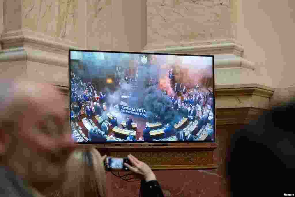 Wartawan menyaksikan siaran langsung di layar televisi saat anggota parlemen oposisi melepaskan granat asap di dalam parlemen Serbia, di ibu kota Beograd. (Reuters)