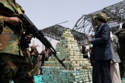 FILE - Houthi followers stand by bills of Yemeni currency during a ceremony held by Houthis to collect supplies for their fighters battling government forces in various front lines, in Sanaa, Yemen, Sept. 24, 2020.
