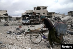 FILE - A man walks with his bicycle through a debris-littered site in the besieged town of Douma, eastern Ghouta, near Damascus, Syria, March 30, 2018.