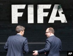스위스 취리히에 소재한 '피파(FIFA)' 본사의 로고 앞에 두 남성이 서 있다.