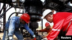 FILE - Men work at an oil pump in Lagunillas, Ciudad Ojeda, in the state of Zulia, Venezuela, March 20, 2015.