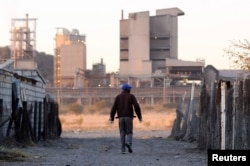 FILE - A township resident walks past Lonmin's Marikana platinum mine, June 13, 2014.