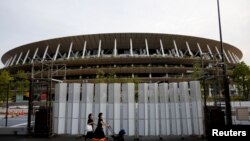 Pejalan kaki yang menggunakan masker pelindung, pasca wabah COVID-19, berjalan di depan Stadion Nasional, stadion utama Olimpiade dan Paralimpiade Tokyo 2020 di Tokyo, Jepang, 7 Juli 2021. (Foto: Reuters)