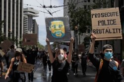 A woman holds a sign showing George Floyd while marching on Market Street at a protest calling for an end to racial injustice and accountability for police in San Francisco, June 20, 2020.