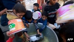 Palestinian children collect food at a donation point provided by a charity group in the southern Gaza Strip city of Rafah, on December 6, 2023, amid continuing battles between Israel and the Palestinian militant group Hamas.