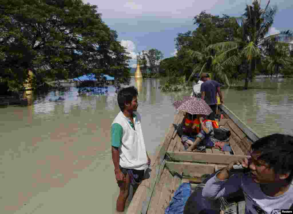 Seorang pria (kiri) berdiri di salah satu atap rumah yang terkena banjir di sebelah perahu media di Kalay, sebuah desa di kawasan Sagaing, Myanmar barat laut, 2 Agustus 2015.