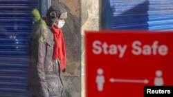 Seorang pejalan kaki mengenakan masker, melewati tanda imbauan untuk menjaga jarak di tengah pandemi Covid-19 di Coventry, Inggris, 25 Oktober 2020. 