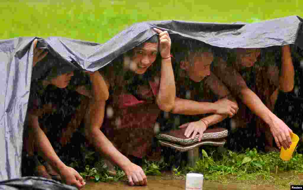 Buddhist monks take shelter under a tarpaulin sheet to protect themselves from the rain as they attend the birthday celebrations of the Tibetan spiritual leader the Dalai Lama (unseen) at Drepung Loseling Monastery in Mundgod, in the southern state of Karnataka, India.