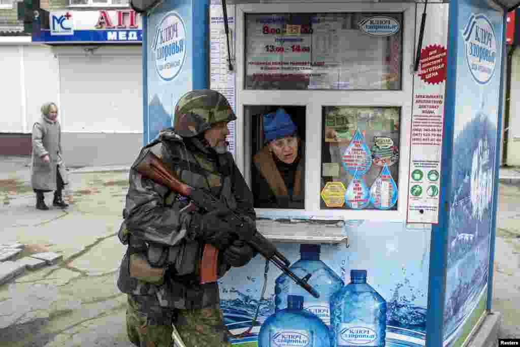 Seorang pemberontak pro-Rusia berlindung sementara seorang perempuan dari dalam kios mengintip, dalam sebuah latihan anti-teroris di Donetsk, Ukraina.
