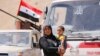 FILE - A Syrian refugee who left Lebanon carries a toddler as she arrives in Qalamoun, Syria, June 28, 2018.