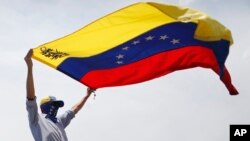 FILE - A masked anti-government protester waves a Venezuelan flag during protests in Caracas, Venezuela, May 1, 2019. 