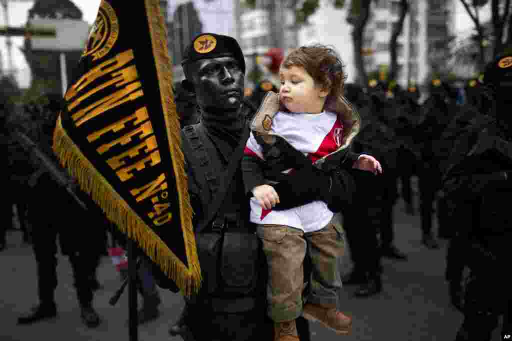 Intor Montoro Carba, a military special forces officer, holds Jeremy Bock for a photo, before the start of a military parade marking the country's Independence Day in Lima, Peru. Peru declared it's independence from Spain in 1821.