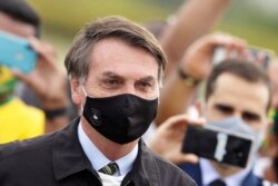 Brazil's President Jair Bolsonaro, wearing a face mask amid the new coronavirus pandemic, stands amid supporters taking pictures with cell phones as he leaves his official residence of Alvorada palace in Brasilia, May 25, 2020.