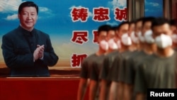 FILE - Paramilitary police officers march in formation near a poster of Chinese President Xi Jinping at the gate to the Forbidden City, in Beijing, China, May 22, 2020.