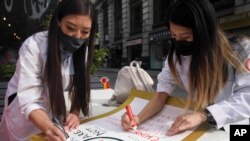 Dr. Michelle Lee, left, a radiology resident, and Ida Chen, right, a physician assistant student, prepare posters they carry at rallies protesting anti-Asian hate, April 24, 2021, in New York's Chinatown.