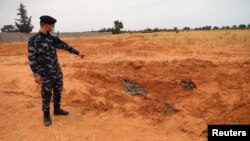 Un membre des forces de sécurité fidèles au GNA pointe vers une fosse commune à Tarhouna, en Libye, le 11 juin 2020.