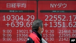 FILE - A man walks past an electronic stock board showing Japan's Nikkei 225 and New York Dow index at a securities firm in Tokyo March 27, 2020. 