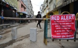 A boy wearing a face mask as a precaution against coronavirus walks past a notice displayed by authorities on a makeshift barricade set up to restrict entry in a containment zone during lockdown in Bengaluru, India, July 5, 2020.