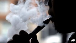 FILE - A man smokes an e-cigarette in Chicago, April 23, 2014. The U.S. government says 3 million middle- and high schoolers reported using e-cigarettes in 2015, an increase from around 2.5 million the year before.