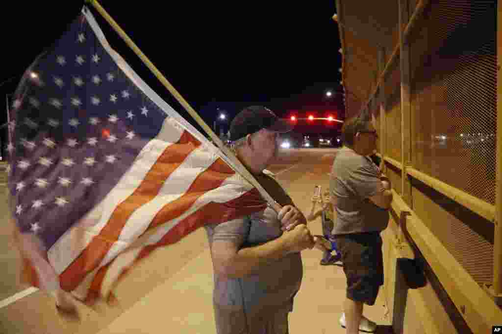 Joe Gruber, of Anthem, Ariz., holds an American flag at an overpass along Interstate 17 as he and dozens of others wait for the procession with the hearse carrying the late Arizona Sen. John McCain, Aug. 25, 2018, in Anthem, Ariz.