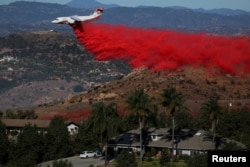 An aircraft drops fire retardant as firefighters take advantage of light winds to attack the Lilac Fire, a fast-moving wildfire in Bonsall, California, Dec. 8, 2017.