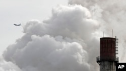 FILE - A passenger airliner flies past steam and white smoke emitted from a coal-fired power plant in Beijing, Feb. 28, 2017.