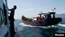 Polisi mengawasi perahu kayu yang membawa pengungsi Rohingya dari Myanmar. Pemerintah Australia mengatakan kebijakan mereka tidak mengijinkan pencari suaka membahayakan keselamatan hidup mereka untuk tiba di Australia dengan menggunakan perahu.
