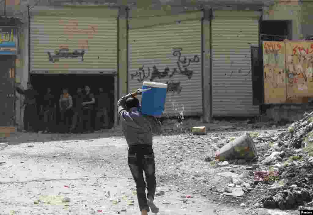 A man holding a water cooler runs to avoid a sniper in Aleppo's Salaheddine neighborhood, April 28, 2013.
