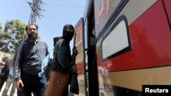 Seorang anggota kelompok pemberontak Suriah dengan bertopeng menaiki bus bersama keluarganya untuk meninggalkan Homs, hari Minggu (21/5). 