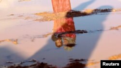 A Syrian refugee woman carrying her son is reflected a puddle of rain water as she stands outside her tent after heavy rain at al-Zaatari refugee camp in the Jordanian city of Mafraq, near the Syrian border, January 10, 2013. 